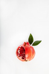 Minimal photo of a cut pomegranate fruit with two fresh leaves on a plain white background, Flat lay contemporary ingredient food art 