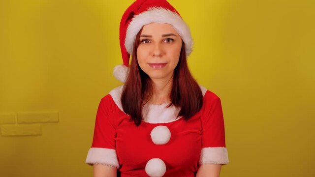 Woman in santa costume on yellow background. Pretty female in christmas hat looking at camera and smiling.