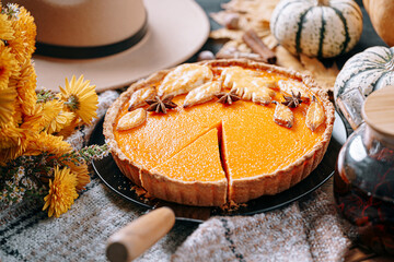 autumn composition with pumpkins, yellow tea flowers, warm plaid and hat and pumpkin pie in the...