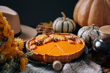 autumn composition with pumpkins, yellow tea flowers, warm plaid and hat and pumpkin pie in the...