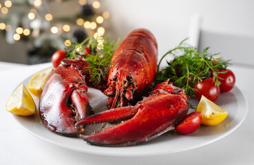 Crop shot of freshly cooked red lobster with vegetables on a plate and white table. Christmas light on a background. Holidays food concept
