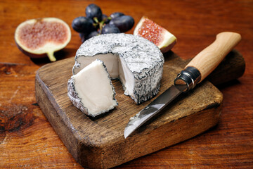 Traditional French Chevre goat milk cheese with fig and grapes offered as close-up on a wooden board