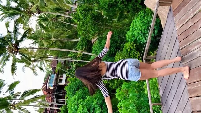 Young girl dance and turns around her head slow on a wooden platform in a striper t-shirt near palm trees and rice Tegalalang terraces on Bali. High quality 4k vertical footage