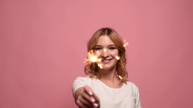 Young woman rejoices and holds a sparkler on a pink background