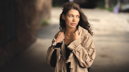 Fototapeta premium Elegant young girl in a beige raincoat posing outdoors