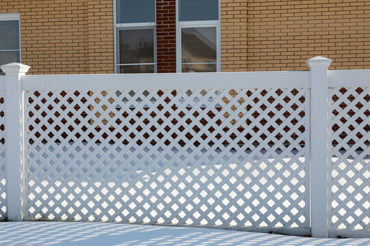 White Plastic Fence In A Modern Cottage Village On A Clear Winter Day. Snow Drifts In Front Of The Vinyl Fence