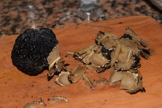 Black truffle being sliced on a wooden cutting board