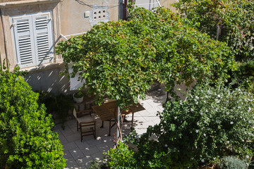 Fototapeta na wymiar Garden and terrace design and landscaping: Cozy garden furniture, chairs, table put on a tiled terrace surrounded by lush mediterranean green plants, bushes, palms which dispense shadow, croatia