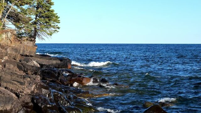 Gorgeous landscape along the rocky and tree lined north shore of Lake Superior in Minnesota on a beautiful sunny day, with white waves rolling in from the blue water.