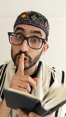 Jewish Bearded Man making silent sing with his finger during pray. The man is wearing a Tallit