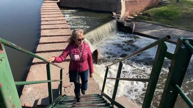 Cheerful adult woman in sunglasses walking up the stairs to the dam gates on a sunny day.