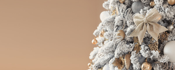 Obraz premium Trendy luxury snowy christmas tree decorated in golden colors on a beige background. Decorations for the new year, a luxurious tree decorated with a gold bow and silver balls. Copy space.