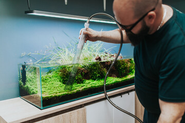 Worker in aquarium showroom changing water in aquarium using siphon. - obrazy, fototapety, plakaty