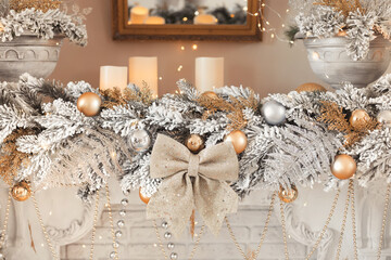 Composition of a christmas garland with candles, silver balls and a golden bow on the fireplace