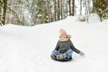 Fototapeta na wymiar Funny little girl having fun with a sleigh in beautiful winter park. Cute child playing in a snow.