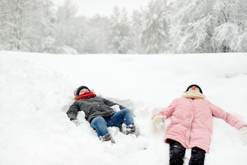 Fototapeta na wymiar Two young girls having fun together in beautiful winter park. Cute sisters playing in a snow. Winter activities for family with kids.