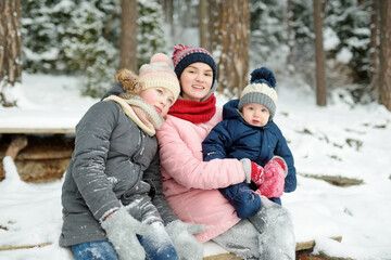 Fototapeta na wymiar Two big sisters and their baby brother having fun outdoors. Two young girls holding their baby boy sibling on winter day. Kids with large age gap.