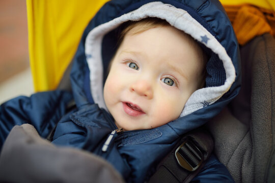 Sweet baby boy wearing warm clothes sitting in a stroller outdoors. Little child in pram. Infant kid in pushchair. Winter walks with kids.