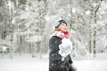 Adorable girl having fun in beautiful winter park during snowfall. Cute child playing in a snow. Winter activities for family with kids.