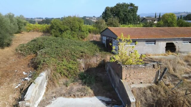 Drone view of old abandoned farmland in ancient Italian province, ruined industrial barn in the middle of isolated medieval village. Farm animals stall with broken windows and rusty doors overgrown