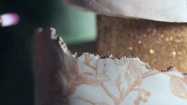 Macro view of baker, decorating the edges of cake with brush.