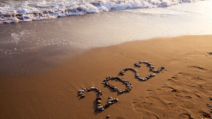 2022 Happy new year concept. Top view of 2022 numbers written on the sand of coastline with wave.Message hand written in golden sand on beautiful sunset or sunrise golden sky background            