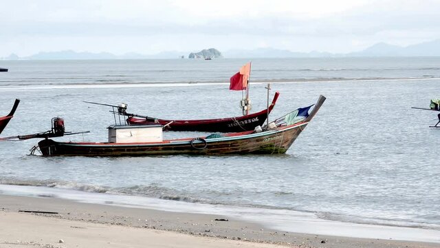 Fishing boats moored along a windswept beach during the day in southern Thailand.