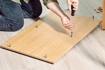 Handyman is assembling flat pack furniture with help of screwdriver.