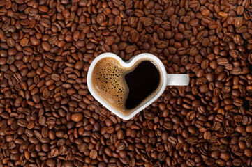 Coffee with a beautiful froth in a mug in the shape of a heart on a background of coffee beans. copy space