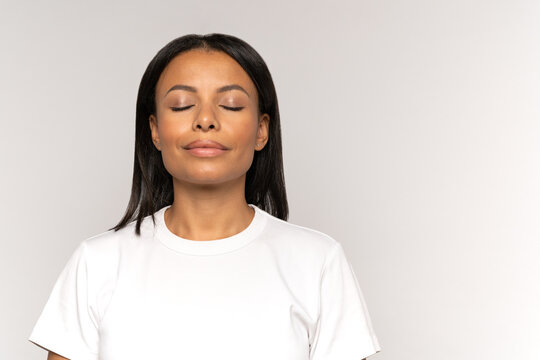 Calm peaceful african american woman with closed eyes and relaxed smile breathing deeply focused on positine thinking and meditating. Young female relaxing or recovering after stress or panic attack