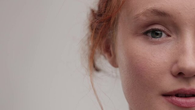 Close up view half face of beautiful young woman Applying Makeup Blush With Brush. Portrait pretty ginger female with nude make look at the camera and smiling. Concept of cosmetology, skincare.