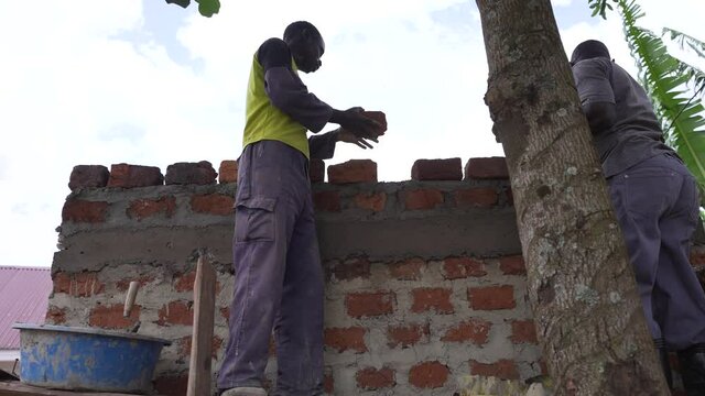 Two African people constructing a traditional house in Africa. Worker Man putting a clay brick on the wall. Rural zone of Uganda.