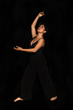 Full Body Portrait Of A Latin Woman Posing Isolated On Black Background, Looking And Stretching Her Arm Up. Female Body Expression Concept.