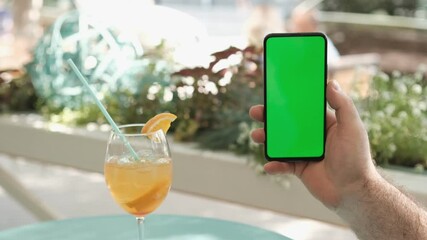 View of female hand holding and pressing on smartphone with mockup green screen in the restaurant european city. Concept of chroma key and greenscreen