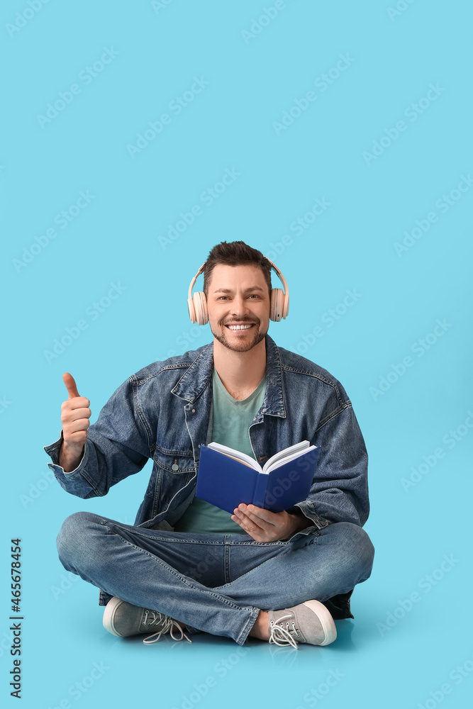 Poster man with headphones and book showing thumb-up on color background