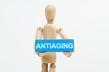 A figurine of a man holds in his hands a blue wooden block with the inscription ANTIAGING. The...