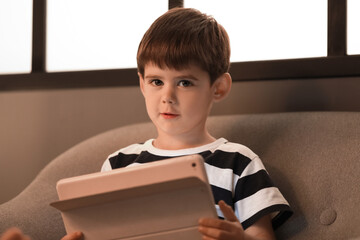 Fototapeta na wymiar Little boy watching cartoons on tablet computer in armchair at night