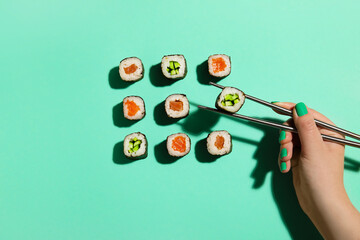 Woman taking maki roll with chopsticks on color background © Pixel-Shot