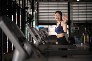 Young Asian woman running on treadmills in sport gym.

