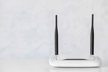 Modern wi-fi router on table near white wall