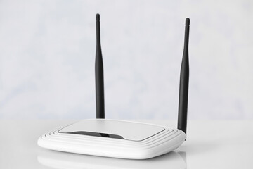Modern wi-fi router on table near white wall