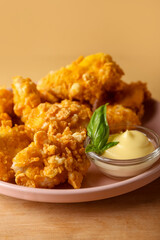 Plate with popcorn chicken, sauce and basil on color background, closeup