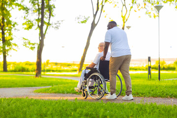 Caregiver and old man in a wheelchair. Professional nurse and patient walking outdoor in the park...