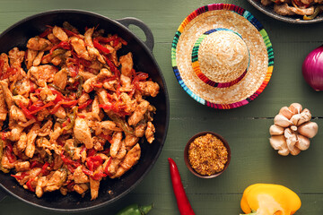 Frying pan with tasty Fajita and sombrero hat on color wooden background