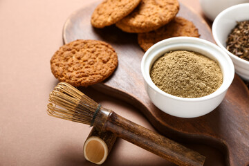 Wooden board with tasty hojicha cookies, powder and chasen on brown background