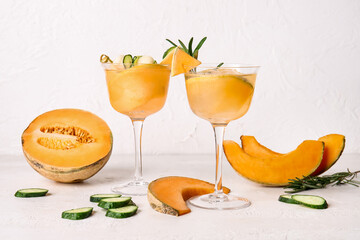 Glasses of cold cocktail, melon and slices of cucumber on light background
