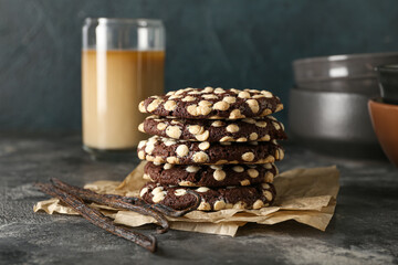 Parchment with delicious chocolate cookies and vanilla sticks on dark background, closeup