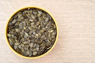 Bowl of pumpkin seeds on the rustic wooden table. Copy space on the right side. Top view. Healthy food concept.