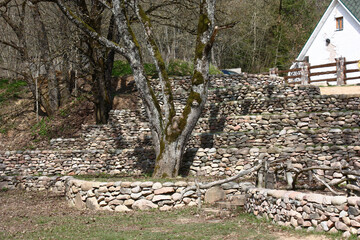 Sunny spring day. On a slope of the hill big trees grow and from a natural stone several retaining...