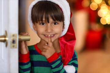 Little boy in Santa hat showing silence gesture at home on Christmas eve
